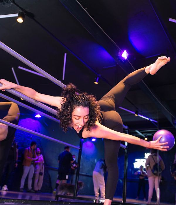 Woman in a fluid yoga pose, demonstrating flexibility and grace in a dark studio with cyan highlights.